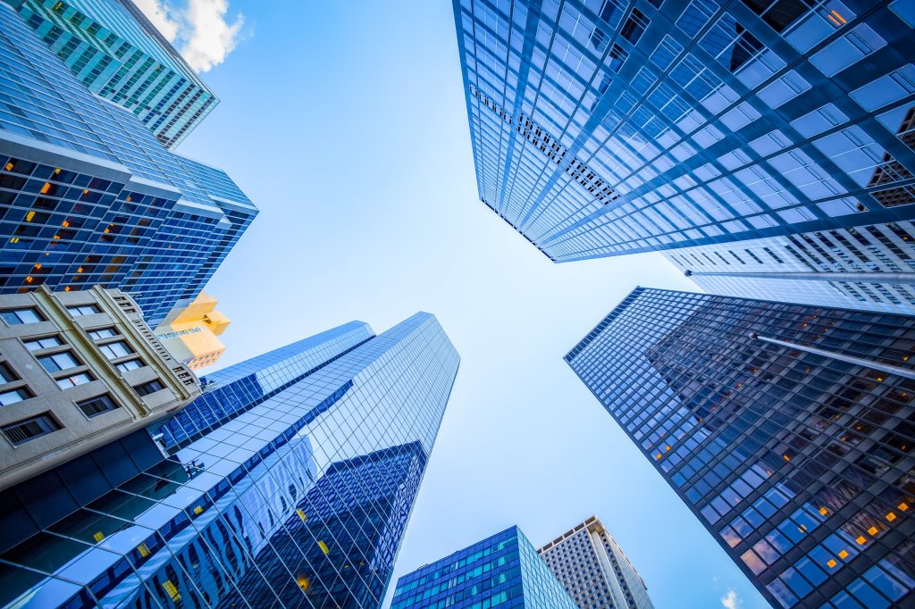 Looking up at modern glass skyscrapers surrounding a clear blue sky.